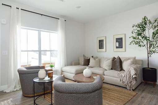 A living room with a grey sofa, a grey armchair, a white table, and a plant.