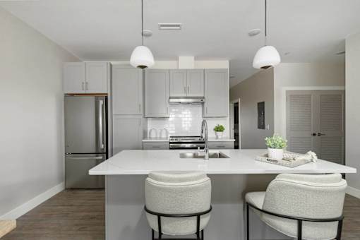 A modern kitchen with a white island and two chairs.
