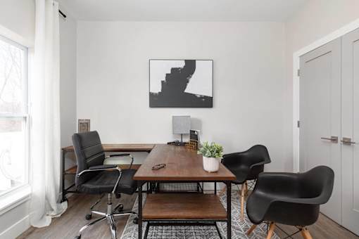 A black and white photo is hanging on a white wall above a black chair and a wooden table.
