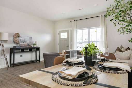 A dining table set with plates and glasses is in the foreground of a modern dining room.