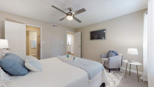 A bedroom with a bed, chair, and ceiling fan.