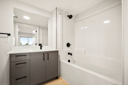 A modern bathroom with a white tub and grey cabinets.