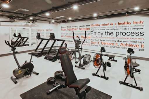 A gym with a variety of exercise equipment and a motivational quote on the wall.
