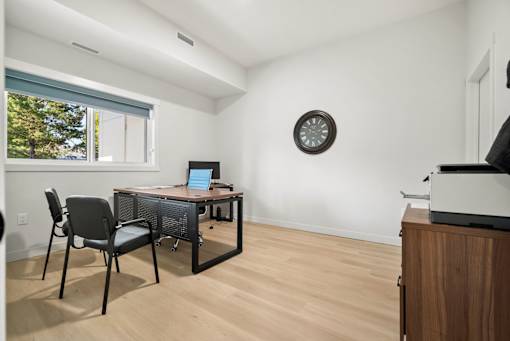 A room with a desk, chairs, and a clock on the wall.