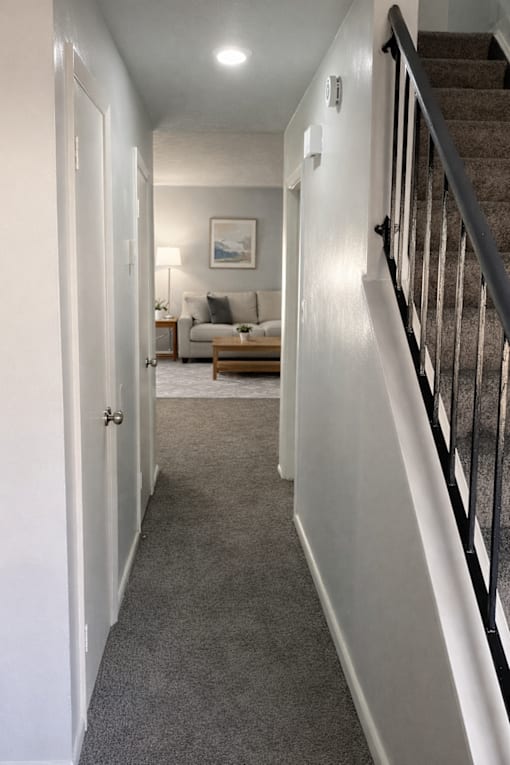 A hallway with a staircase on the right and a couch in the background.