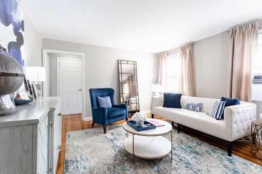 A blue chair sits in a white room with a white couch and a round coffee table.
