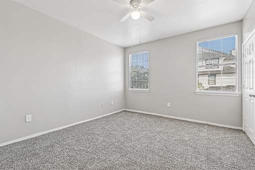 A room with a ceiling fan and two windows.