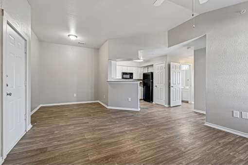A spacious room with wood flooring and a kitchenette in the background.