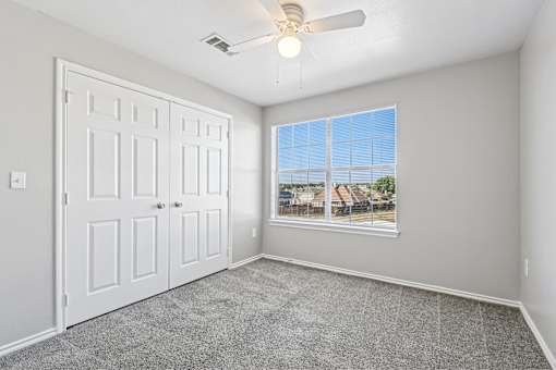 A room with a white door, a ceiling fan, and a window showing a view of houses.