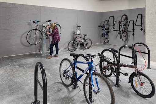 A woman is standing next to a bike in a room with several bikes on the wall. at Ravello Apartments, Redmond, WA