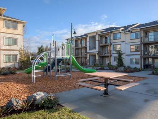 A playground with a green slide and a picnic table in front of apartment buildings. at Mill Creek Meadows Apartments, Mill Creek