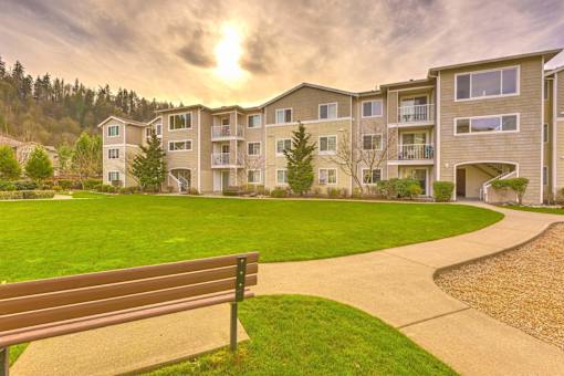 A bench is in the foreground of a grassy area in front of apartment buildings at Valley Springs Apartments, Renton, WA, 98058