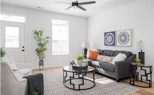 A living room with a grey couch, a black and white patterned rug, and a ceiling fan.