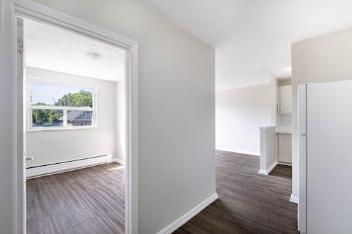 A room with white walls and wooden flooring with a doorway leading to another room.