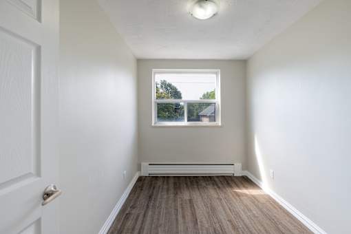 A white door opens to a room with a window and a wooden floor.