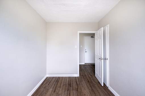 A room with a white door and brown flooring.