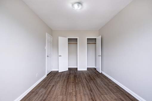 A room with white walls and wood flooring with three white doors.