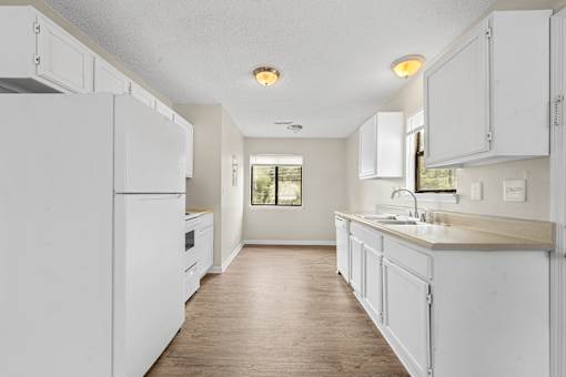A white kitchen with wooden floors and white appliances.