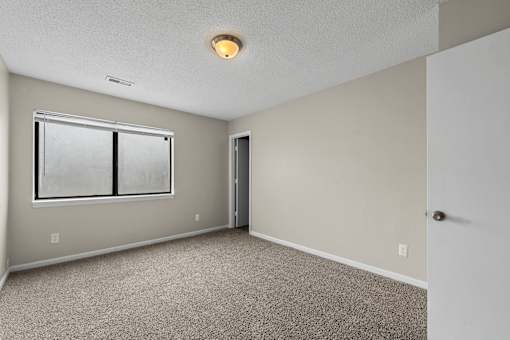 A room with a carpeted floor, a window, and a door.