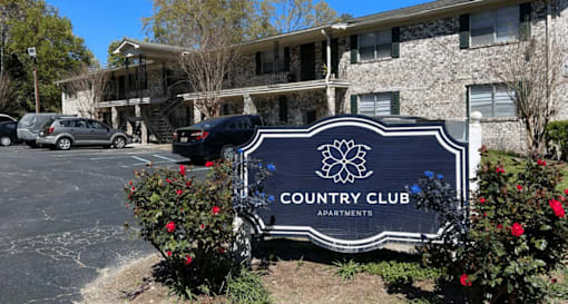 A sign for Country Club Apartments is in front of a building.