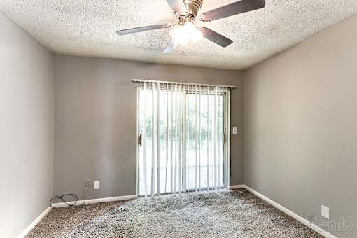 A room with a ceiling fan, a carpeted floor, and a sliding glass door leading outside.