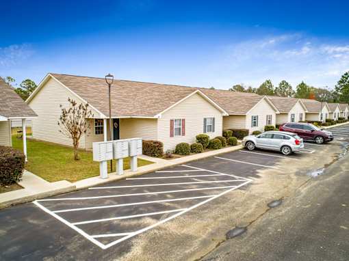 A parking lot with a white car parked in front of a residential building and mailboxes.
