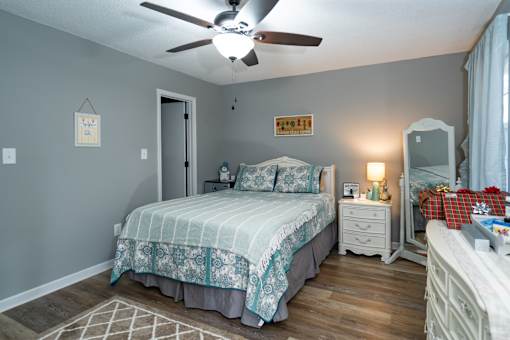 A bedroom with a bed, nightstand, dresser, and a ceiling fan.