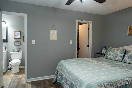 A bedroom with a bed, a fan, and a bathroom next to it.