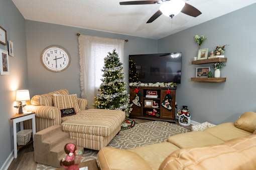 A living room with a couch, chair, Christmas decorations, and a flat screen TV.