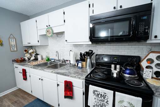 A kitchen with a black stove top oven, a microwave, and white cabinets.