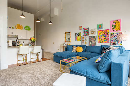 A living room with a blue couch and a kitchen area in the background.