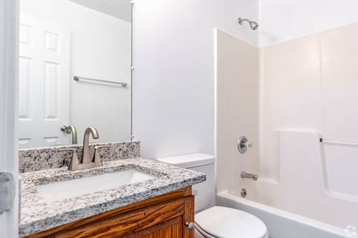A white bathroom with a marble countertop and a toilet.