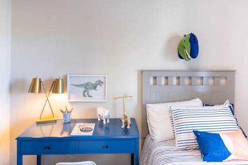 A blue desk with a lamp and a dinosaur picture on the wall.