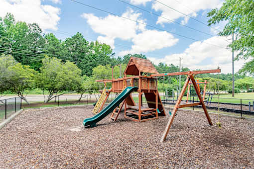 A playground with a green slide and a wooden swing set.