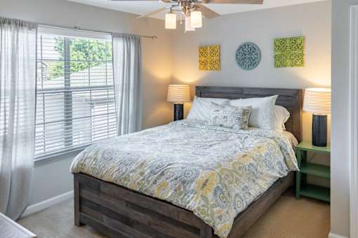 A bedroom with a bed, a ceiling fan, and a window with curtains.