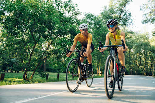Two cyclists wearing helmets and sunglasses ride their bikes on a road.