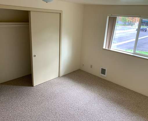 A room with a carpeted floor, a window, and a door.