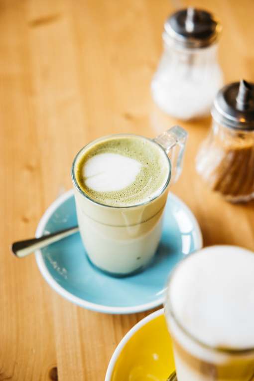 A cup of green tea latte with milk on a saucer.