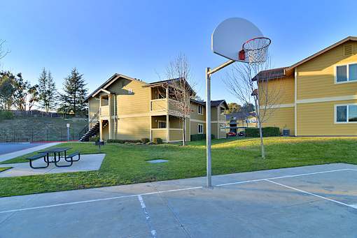A basketball court with a hoop and a bench in front of apartment buildings.
