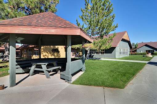 A pavilion with picnic tables is surrounded by green grass.