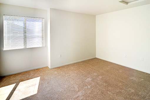 A room with a carpeted floor and a window with blinds.