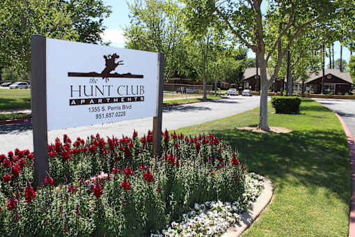 A sign for The Hunt Club Apartments stands in front of a flower bed.
