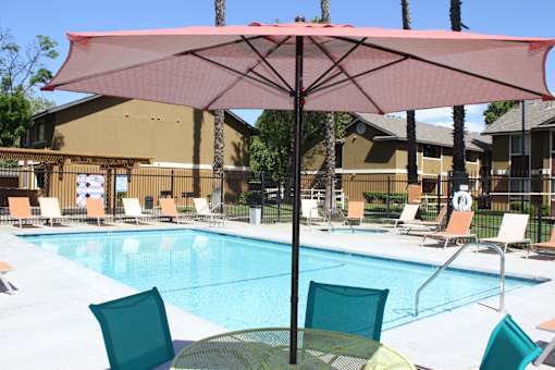 A pool with a red umbrella and chairs around it.
