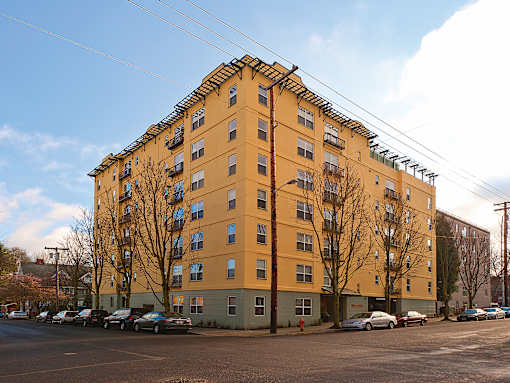 A yellow building with a green base and a parking lot in front.