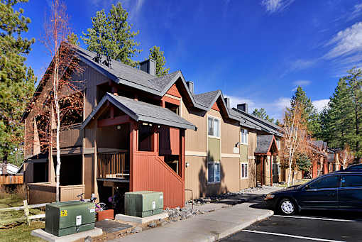 A black car is parked in a parking lot in front of a two-story house.
