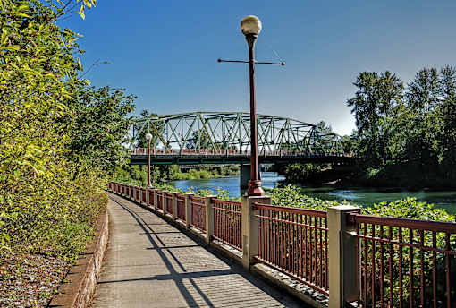A bridge over a river with a metal railing and a lamp post on the sidewalk.