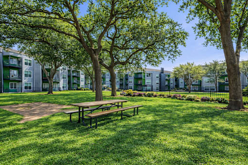 A park with a picnic table and trees in front of apartment buildings. at Infinity on the Landing Apartments , Euless, 76040