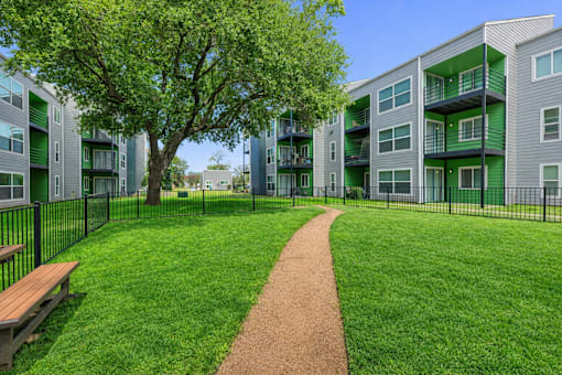 A tree in a grassy area in front of apartment buildings. at Infinity on the Landing Apartments , Euless, TX, 76040