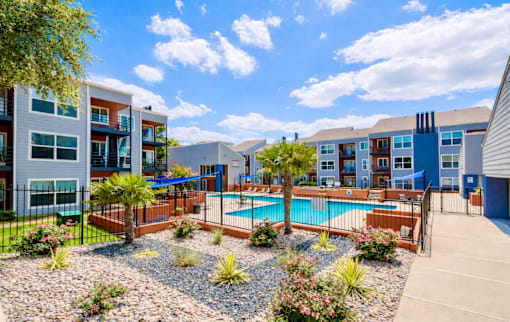 A pool surrounded by a gravel area and a fence with a building in the background. at Infinity on the Landing Apartments , Euless, TX, 76040