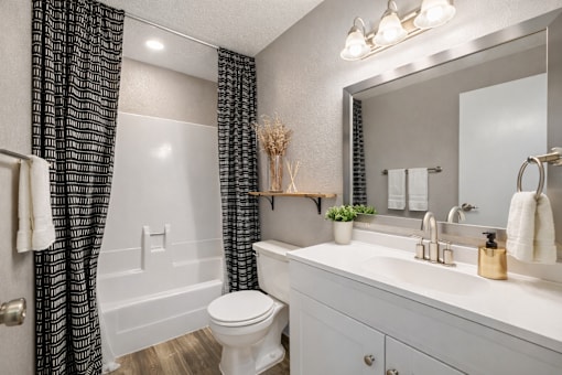 A white toilet is in a bathroom with a white sink and a mirror. at Infinity on the Landing Apartments , Texas, 76040